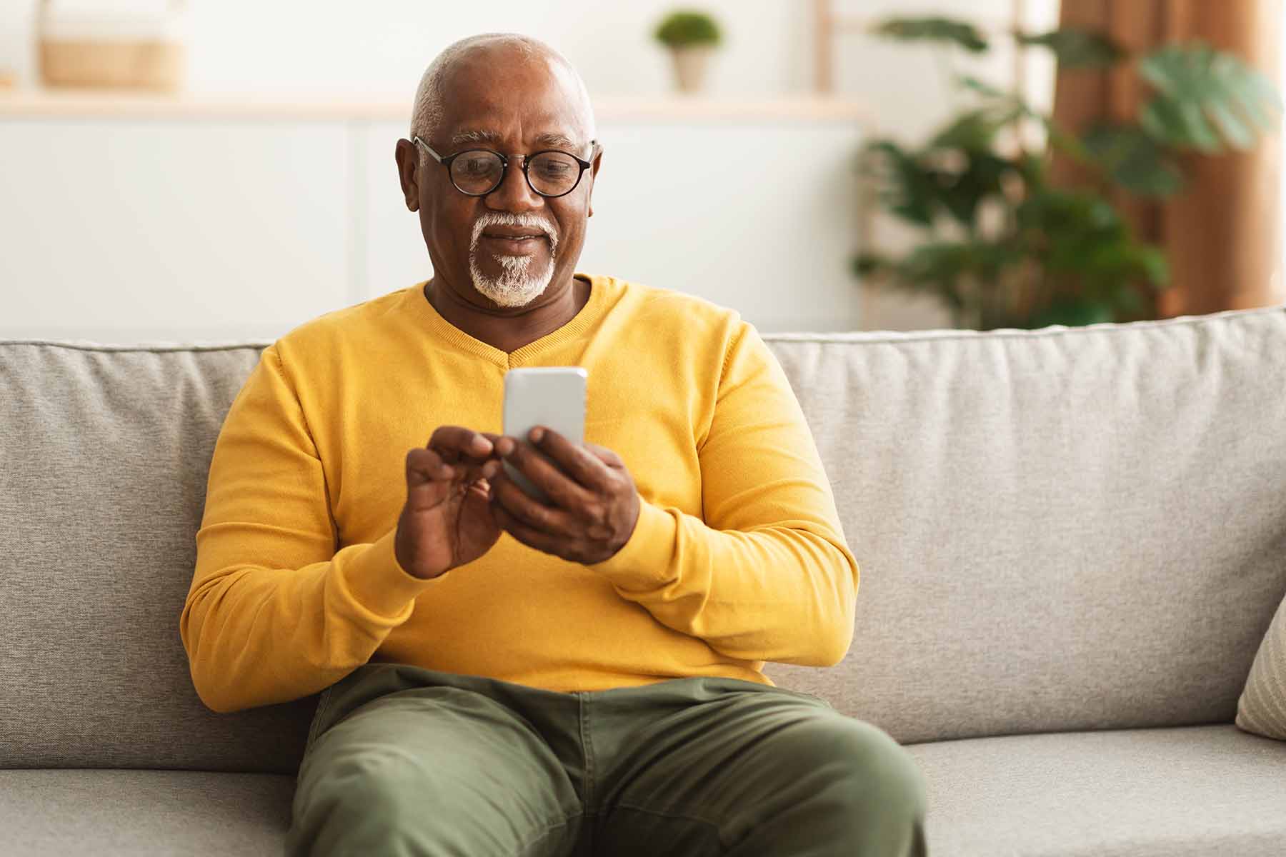 older man sitting on a couch typing into a cellphone