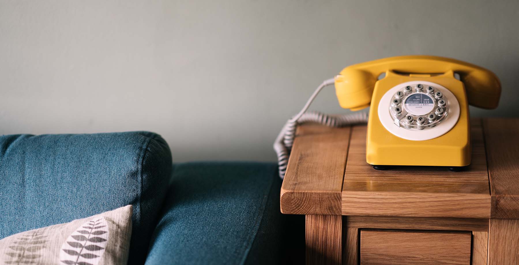Yellow rotary phone sits on side table next to a couch